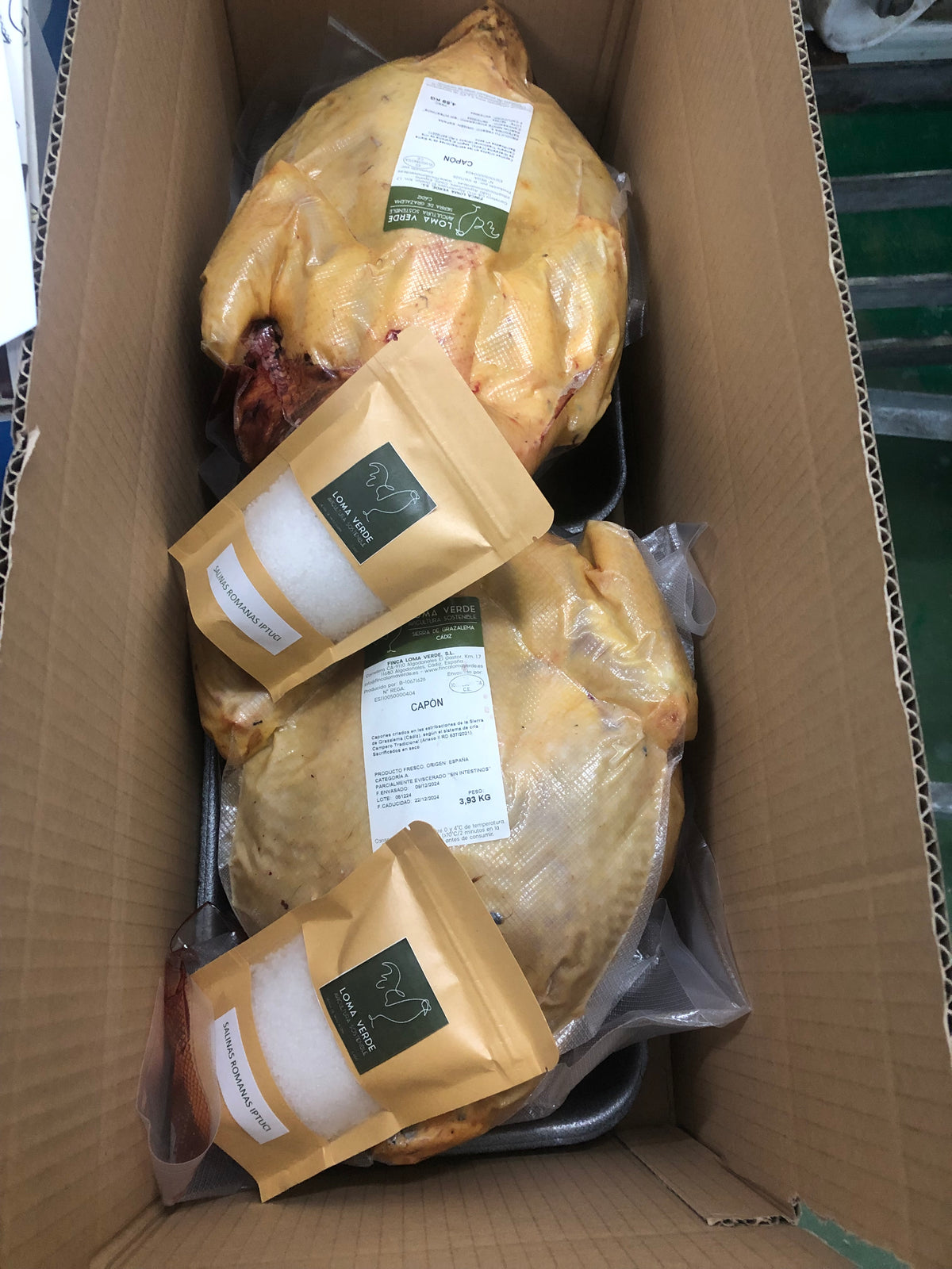 Dos capones Loma Verde parcialmente eviscerados, que conservan la cabeza, envasados al vacío en la caja de envío